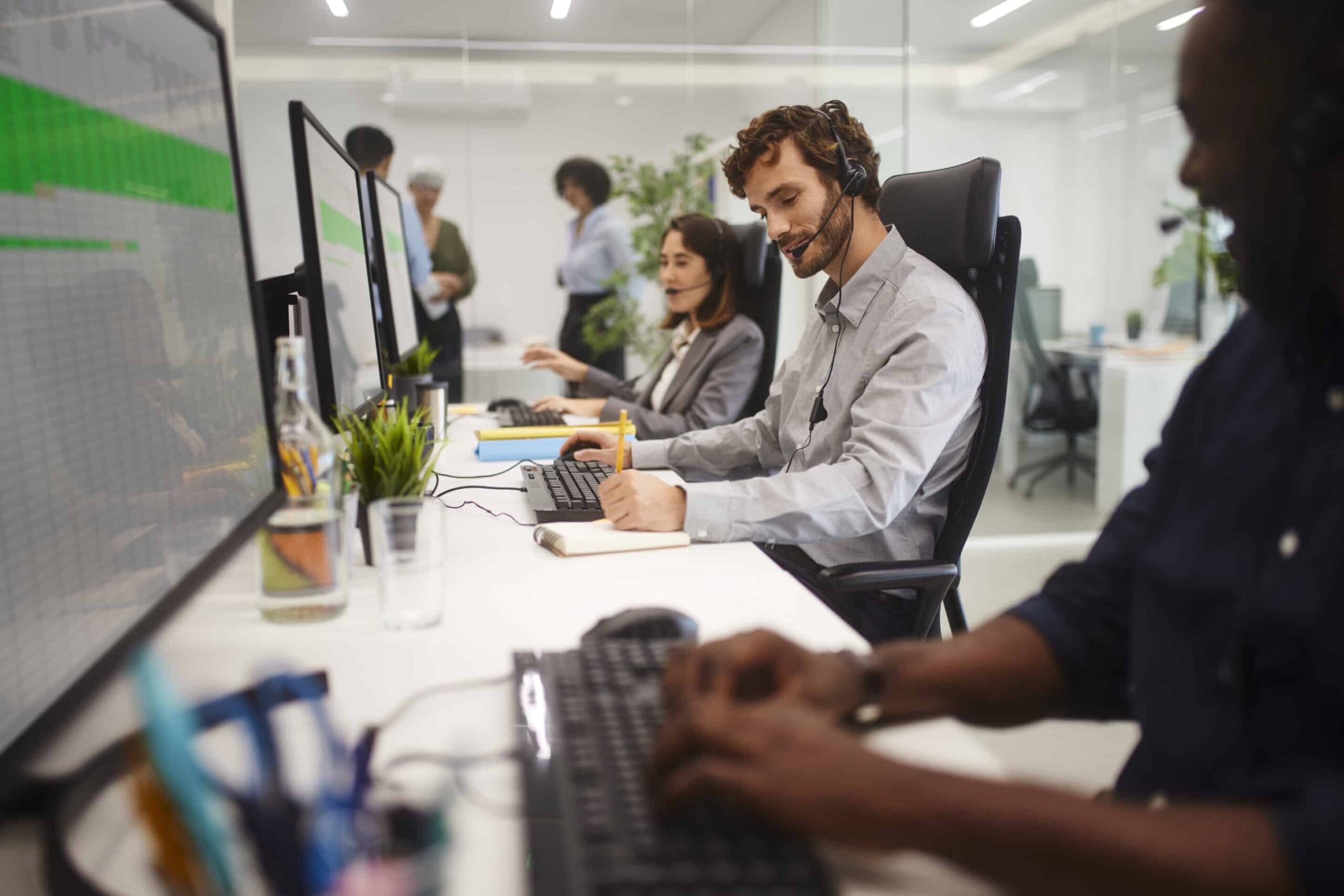 Man and colleagues wearing headset working on call center writing on notepad