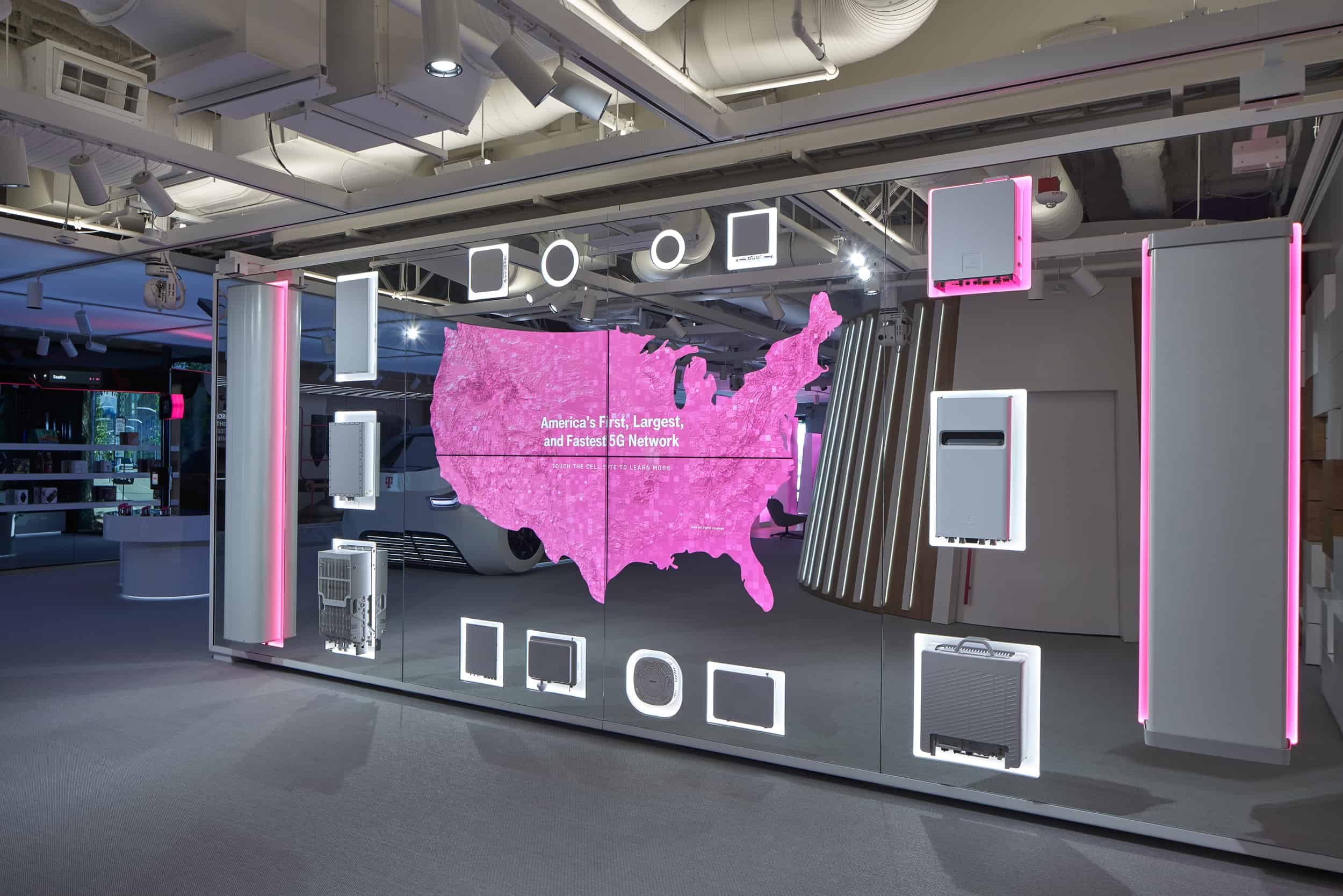 A showroom displays a magenta U.S. map on screen, promoting 5G, with various telecom devices in a sleek, well-lit space.