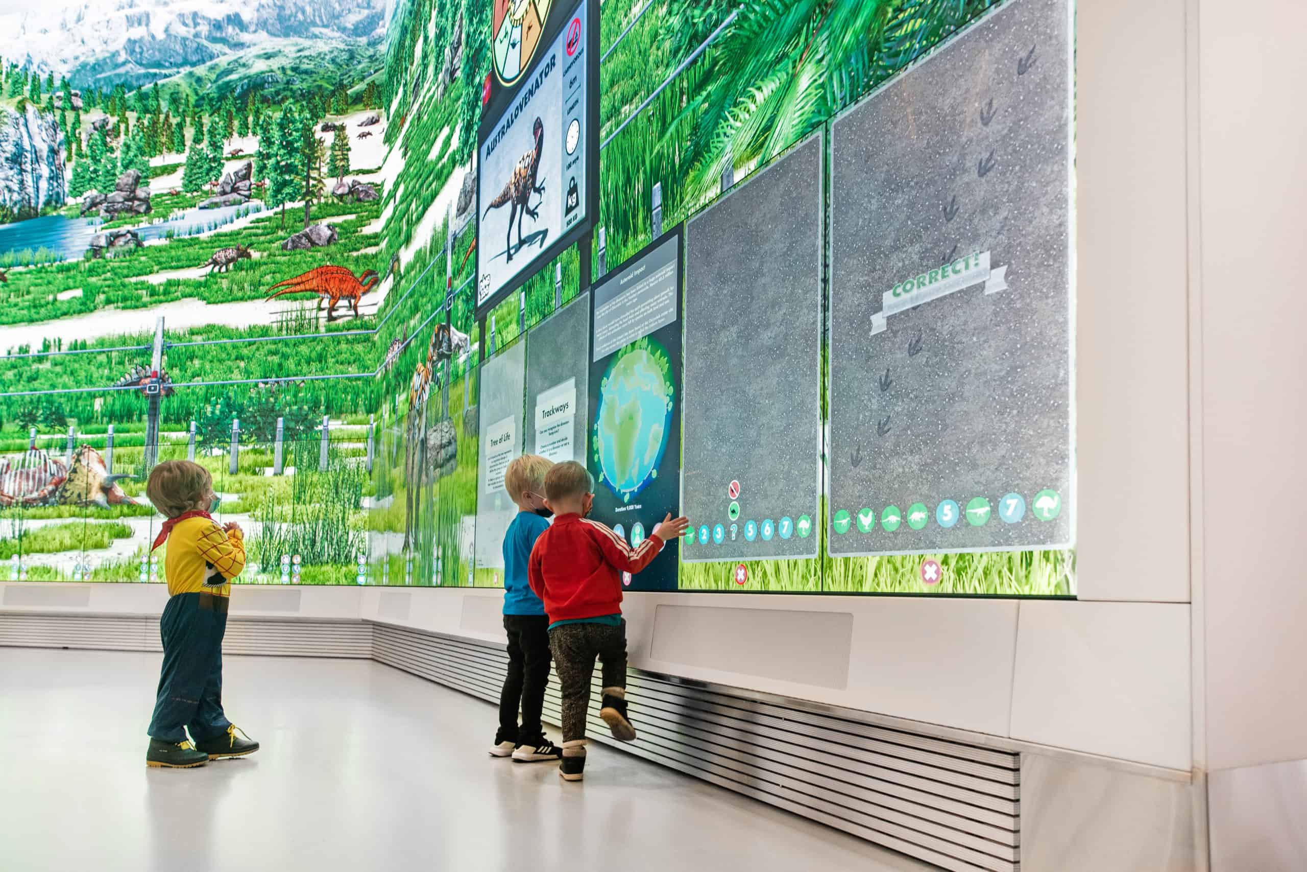 Kids engaged with interactive digital display of dinosaurs, exploring vibrant prehistoric scenes and educational content.