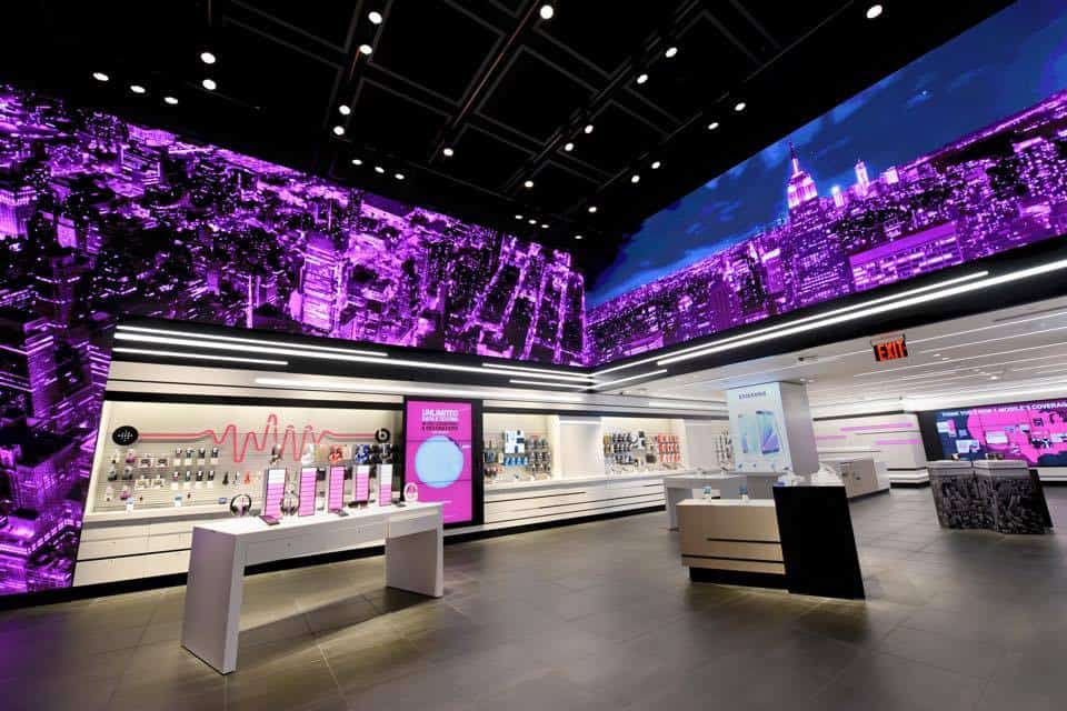 Modern retail store with pink/blue lighting, cityscape walls, sleek dark floor, and displays of electronic devices.