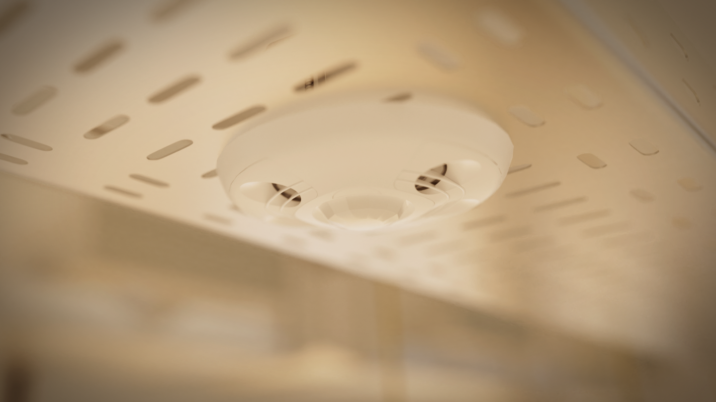 Close-up of a Crestron Occupancy Sensor on a perforated ceiling; vents and central sensor in focus, background softly blurred.