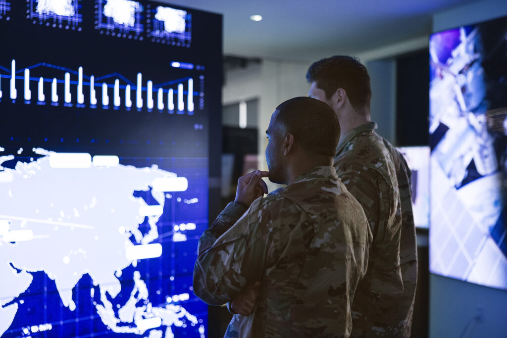 two soldiers in front of command center video wall with map